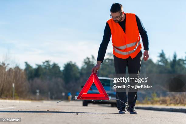 a man putting a warning triangle behind his car - road assistance stock pictures, royalty-free photos & images