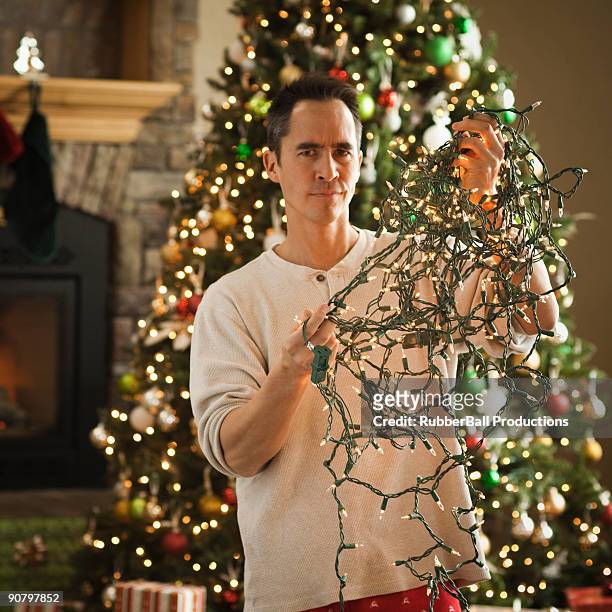 man untangling christmas tree lights - tangled stock pictures, royalty-free photos & images
