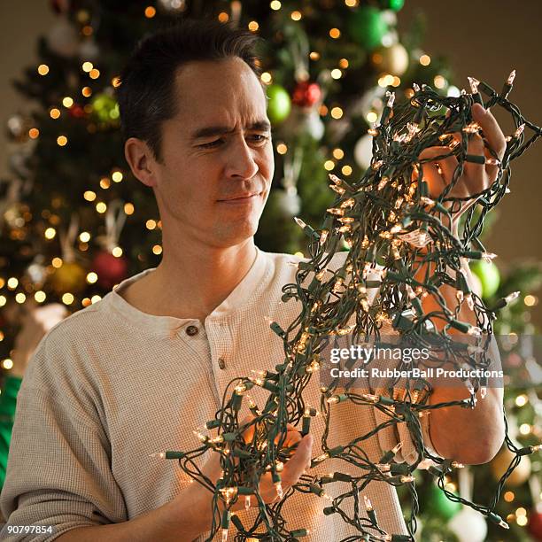 man untangling christmas tree lights - tangled stock pictures, royalty-free photos & images