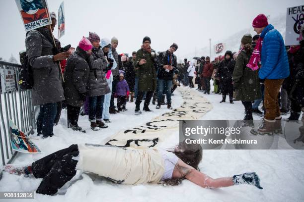 Nina Kaufman of Salt Lake, rolls in the snow, revealing a sheet with a saying on it as eople gather at City Park for the event, Respect Rally during...
