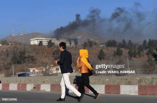 Afghans walk near the Intercontinental Hotel as smoke billows during a fight between gunmen and Afghan security forces in Kabul on January 21, 2018....