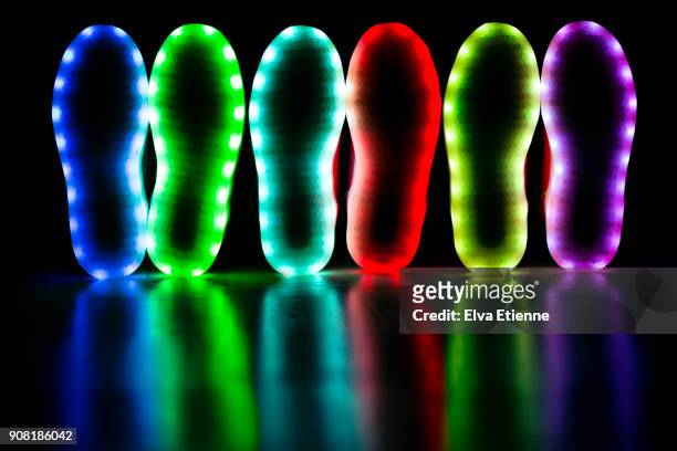 glowing soles of three pairs of led lit shoes - paarse schoen stockfoto's en -beelden