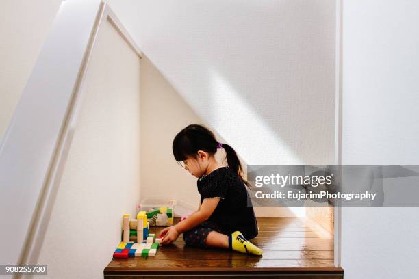 cute little girl playing with wooden toy blocks on indoor stairs - おもちゃ　家 ストックフォトと画像