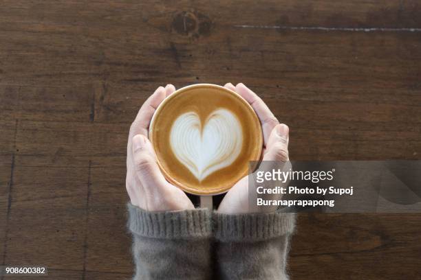 coffee cup in coffee shop.female hands holding cup of coffee on wooden table background - chocolate heart stock-fotos und bilder