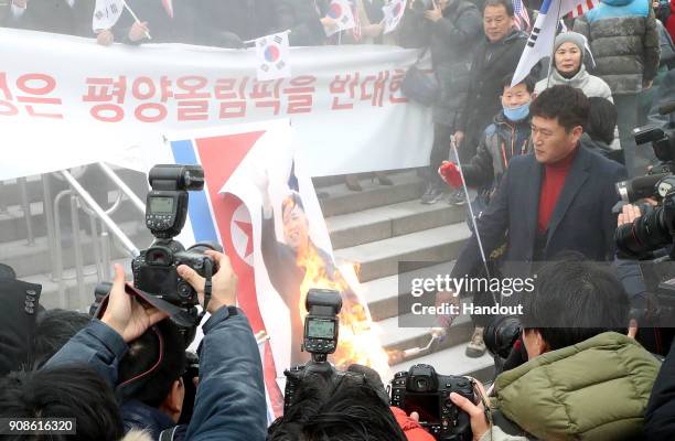 Anti-North Korea activists burn a portrait of North Korean leader Kim Jong-Un during a rally as a North Korean delegation arrives at the station on...