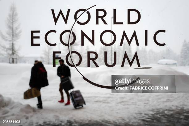 Two people leave the Congress Centre under snow ahead of the opening of the World Economic Forum 2018 annual meeting, on January 22, 2018 in Davos,...