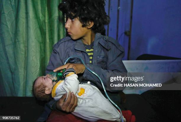 Syrian boy holds an oxygen mask over the face of an infant at a make-shift hospital following a reported gas attack on the rebel-held besieged town...