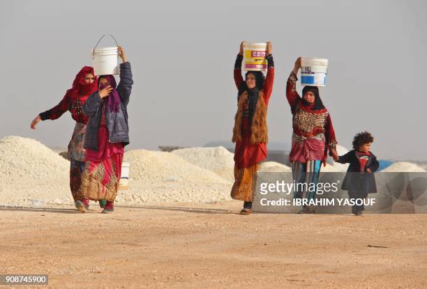 Syrian women whose families fled the bombardment of the southern Idlib and Aleppo countryside carry jugs of water as they walk at a newly-opened camp...