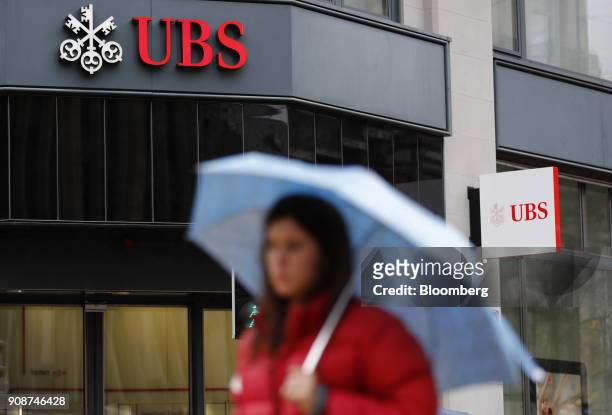 Pedestrian shelters under an umbrella while passing a UBS Group AG bank branch in Zurich, Switzerland, on Monday, Jan. 22, 2018. A UBS loan backed by...