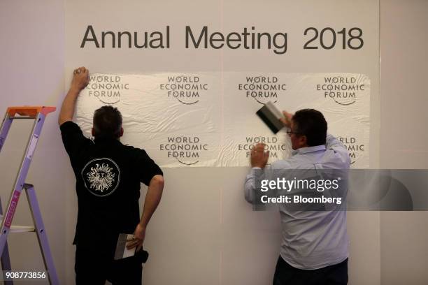 Workers mount World Economic Forum logo transfers onto a background during preparations inside the Congress Center ahead of the World Economic Forum...