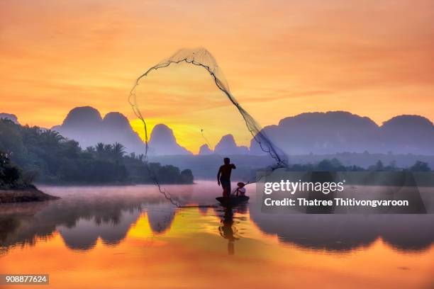 silhouette fisherman a silhouette fisherman throw a net to catch a fish in a river with morning sun. - phang nga bay stock pictures, royalty-free photos & images