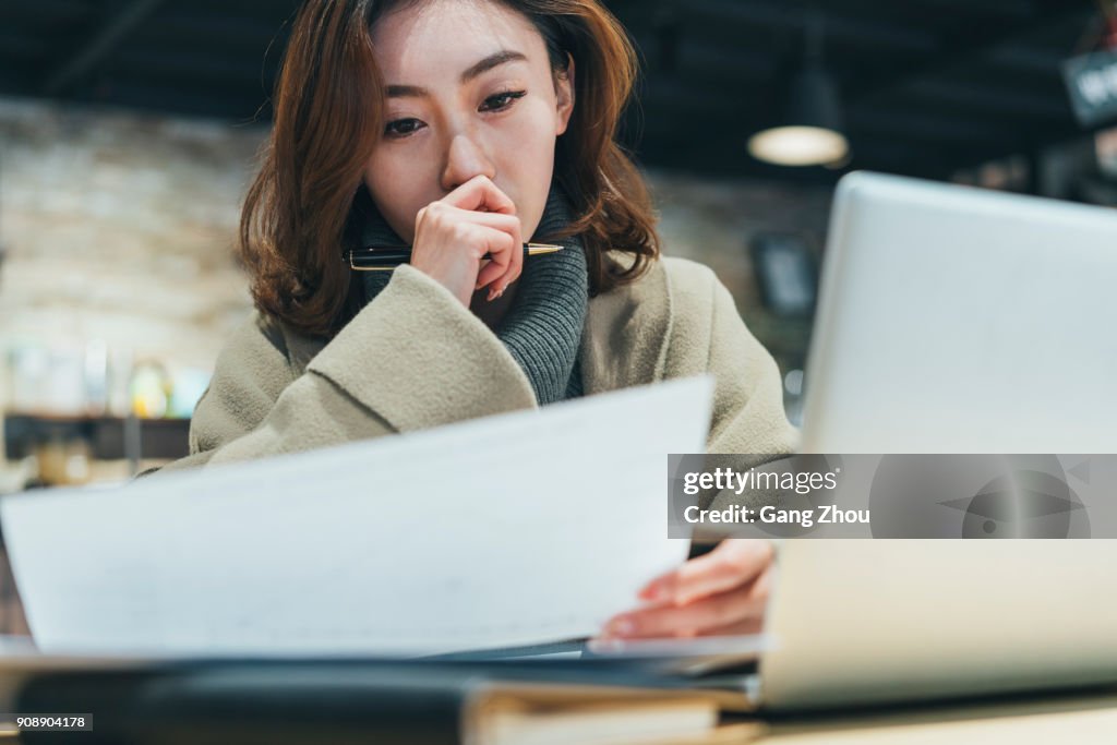 Woman doing paperwork with laptop in coffee shop