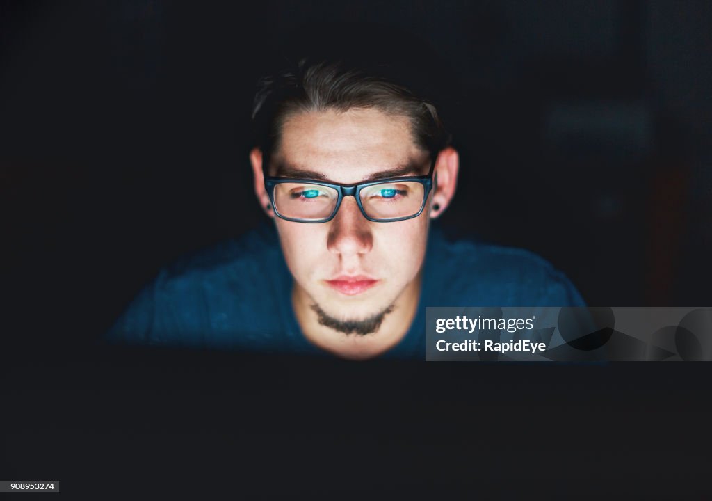 Young man stares intently at computer monitor at night