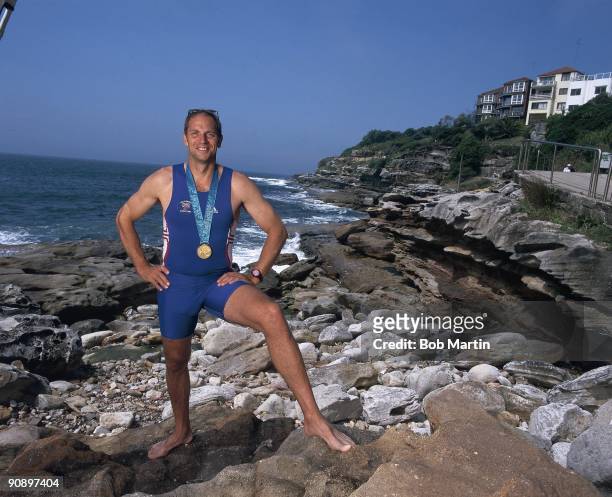 Summer Olympics: Portrait of Great Britain Steven Redgrave victorious with Men's Coxless Four gold medal while standing on top of rocks at beach...