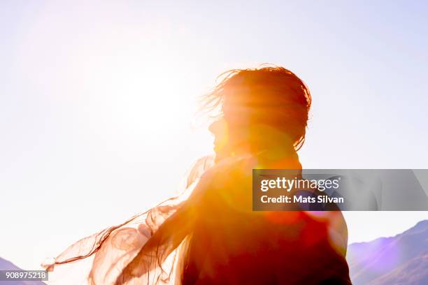 woman with moving hair and scarf in sunlight in a windy day - sunny stock-fotos und bilder