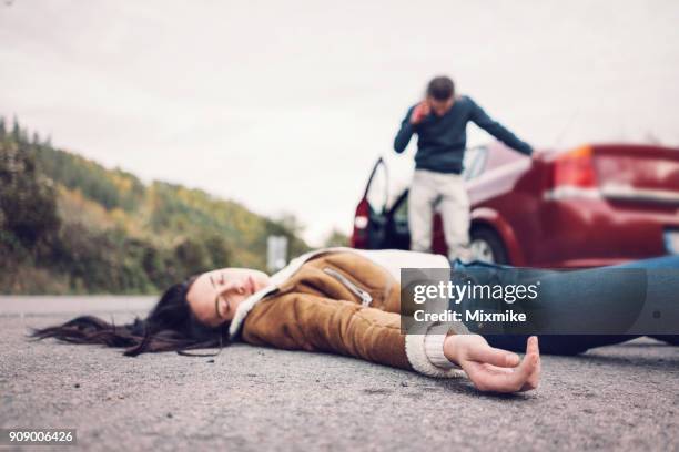 brunette woman on the foreground lying unconscious on the road. - dead bodies in car accident photos stock pictures, royalty-free photos & images