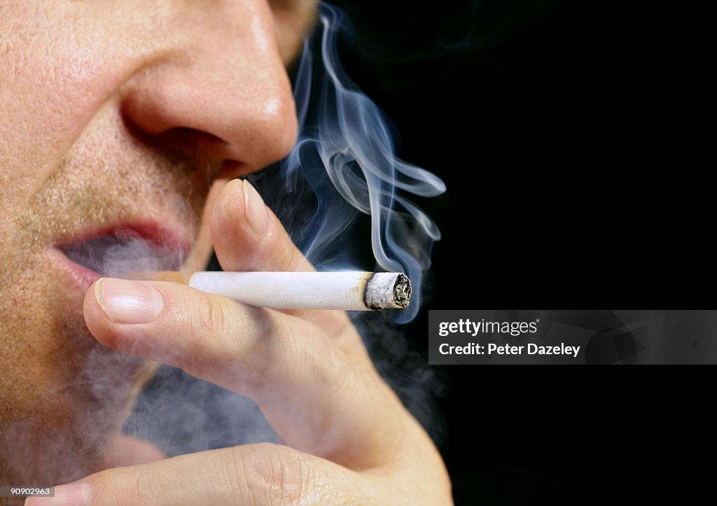 Senior male smoking cigarette on black background
