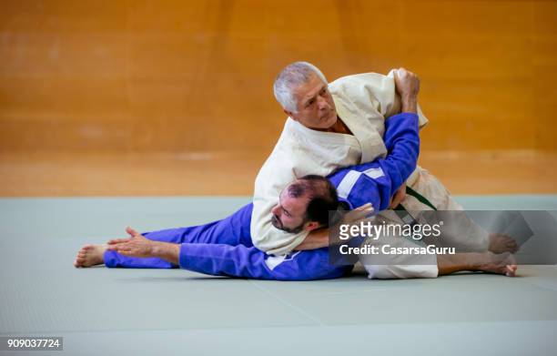 senior judoist holding zijn tegenstander op de grond - asian indoor & martial arts games stockfoto's en -beelden