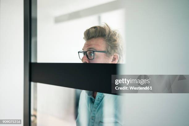 wide-eyed businessman behind glass pane in office - peek fotografías e imágenes de stock