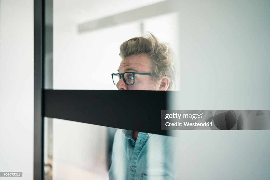 Wide-eyed businessman behind glass pane in office