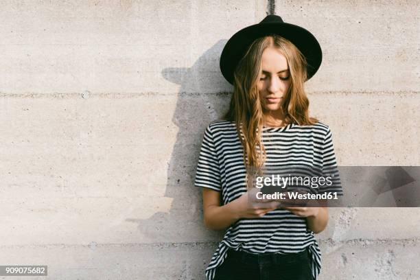 portrait of fashionable young woman wearing hat using smartphone - generazione y foto e immagini stock