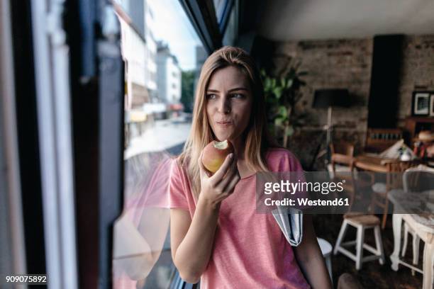 young woman leaning on window, eating apple - speisen und getränke stock-fotos und bilder