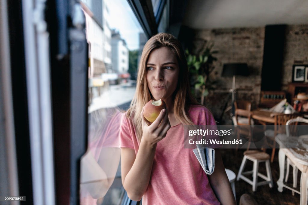 Young woman leaning on window, eating apple