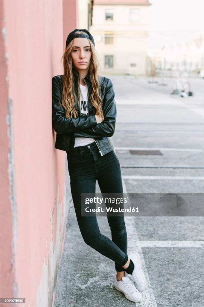 Fashionable young woman wearing baseball cap leaning against wall