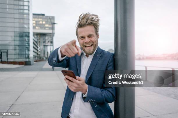 portrait of happy businessman with cell phone in the city - auslachen blick in die kamera stock-fotos und bilder