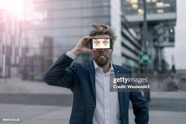 playful businessman holding cell phone in front of his eyes - 40's rumpled business man stockfoto's en -beelden