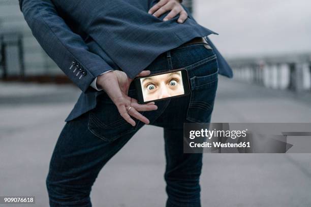 businessman holding cell phone with image of eyes behind his buttocks - rear end imagens e fotografias de stock