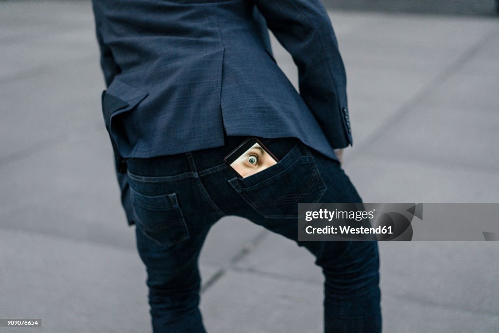 Businessman with cell phone with image of eyes in his trouser pocket
