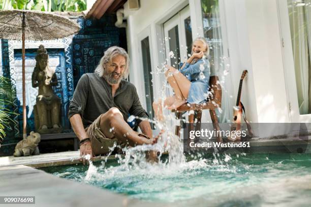 senior man taking selfie at poolside while his wife is playing the guitar - cooler opa stock-fotos und bilder