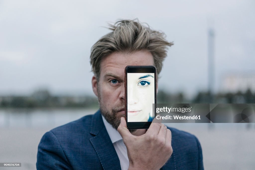 Businessman holding cell phone with image of a woman in front of his eyes