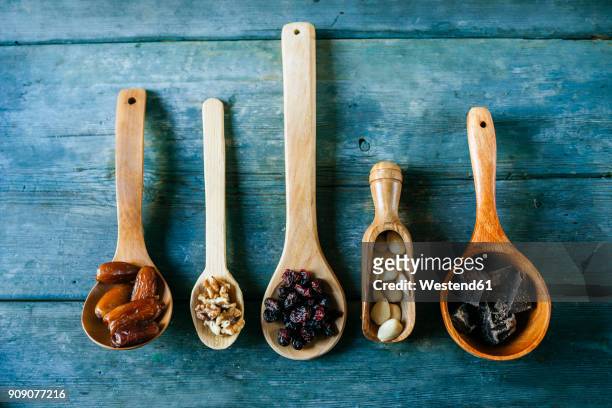 row of different wooden spoons with dates, walnuts, currants, almonds and dark chocolate - dried fruit foto e immagini stock