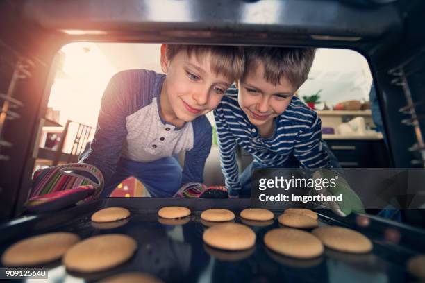 kleine jungen, die cookies aus dem ofen herausnehmen - children only stock-fotos und bilder