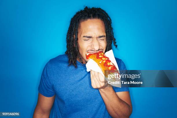 young urban man eating hotdog - hotdog stock-fotos und bilder