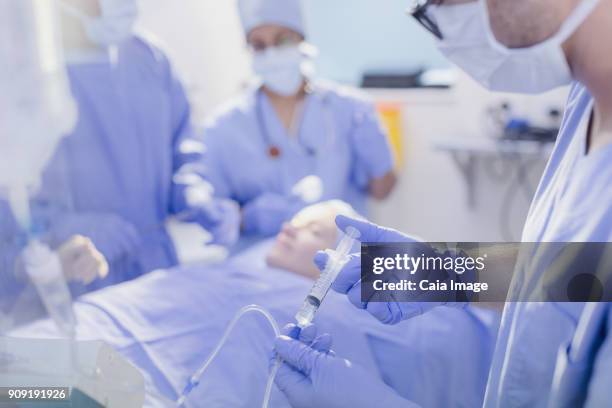 anesthesiologist with syringe injecting anesthesia into iv drip in operating room - inserting iv stock pictures, royalty-free photos & images