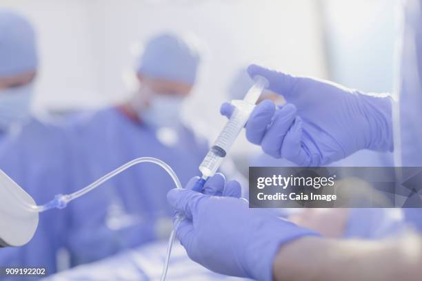 close up anesthesiologist with syringe injecting anesthesia medicine into iv drip in operating room - inserting iv stock pictures, royalty-free photos & images