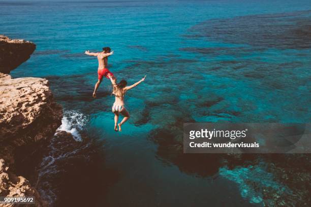 giovane coppia di subacquei coraggiosi che saltano dalla scogliera nell'oceano - clima tropicale foto e immagini stock