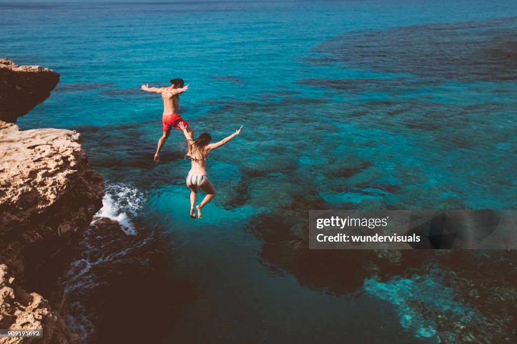 Young brave divers couple jumping off cliff into ocean