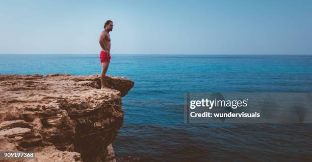 man die op de rand van de klif klaar om te springen in de zee - standing water stockfoto's en -beelden