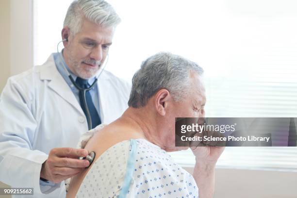 male doctor examining patient in hospital gown - husten stock-fotos und bilder