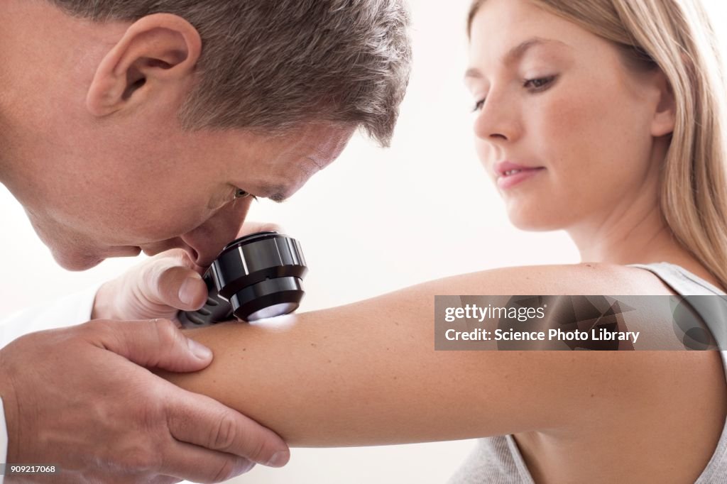 Doctor examining mole on young womans arm