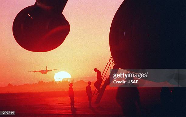 Hercules aircraft takes off in the distance as a section of a Military Airlift Command C-5B Galaxy aircraft, foreground, is silhouetted by the...