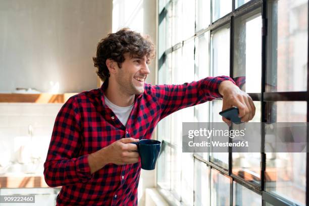 young entrepreneur standing in company kitchen, drinking coffee - café homme vitre photos et images de collection