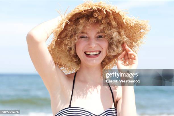 portrait of laughing young woman wearing straw hat on the beach - frau sommer porträt stock-fotos und bilder