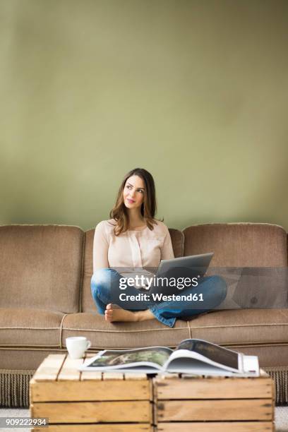 smiling young woman sitting on couch using laptop - mirada de reojo fotografías e imágenes de stock