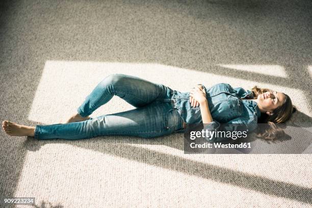 young woman lying on carpet in the living room enjoying sunlight - ropa tirada en el suelo fotografías e imágenes de stock