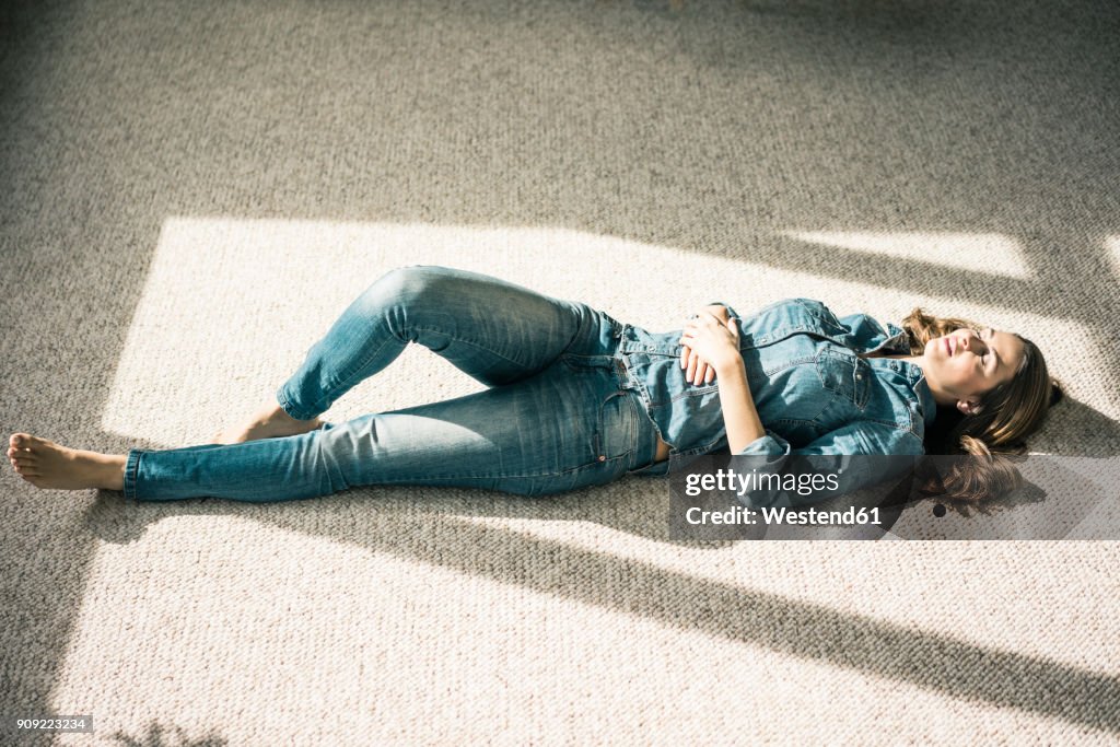 Young woman lying on carpet in the living room enjoying sunlight